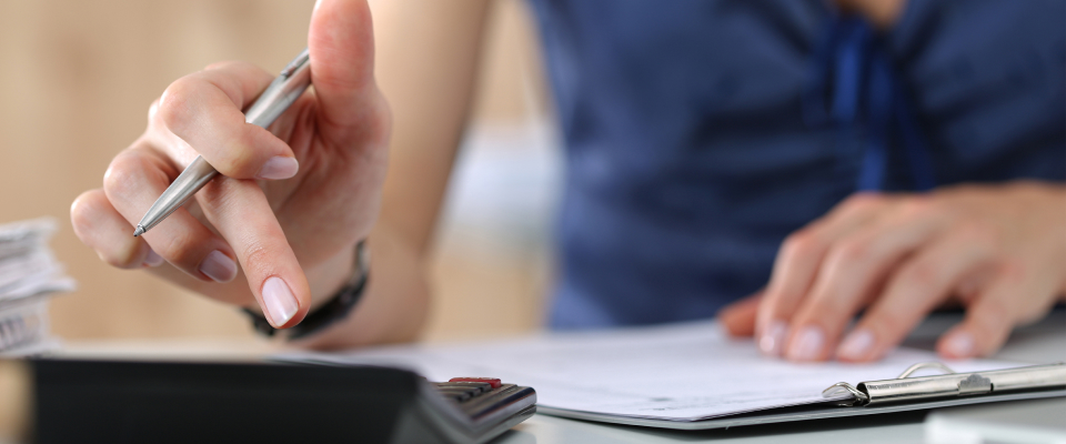 Female punching numbers into a calculator while a clipboard is in front of her on desk